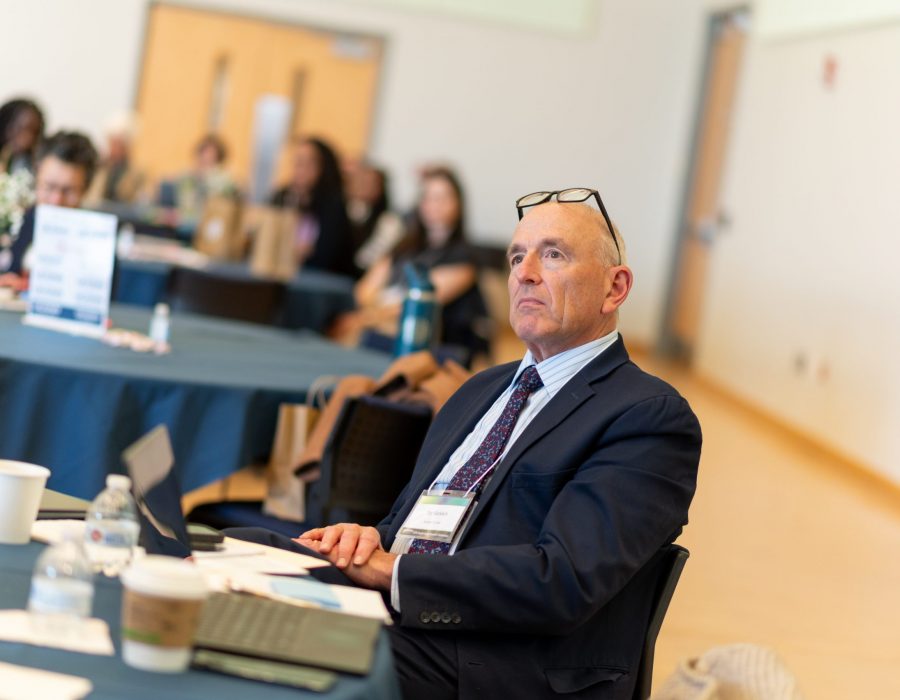 man in suit sits at table listens to presentation